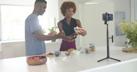 Couple vlogging healthy breakfast presenting berry granola bowl on camera tripod