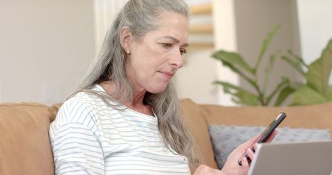 Senior Woman Multitasking with Smartphone and Laptop at Home