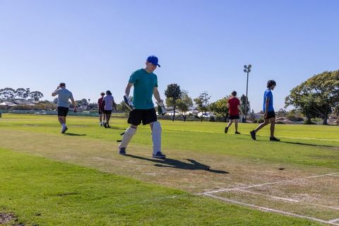 Male cricket teammates walking across suburban pitch during sunny training wearing pads