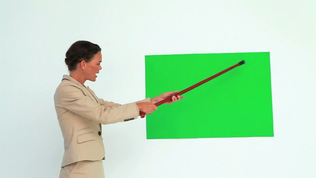 Woman in business attire using a pointer stick to discuss or explain concepts on a green screen, ideal for presentations, educational materials, and corporate training videos.