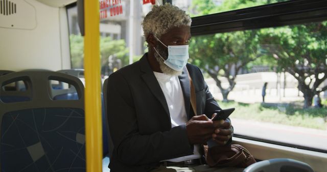 African american senior man wearing face mask using smartphone while sitting in the bus. hygiene and social distancing during coronavirus covid-19 pandemic.