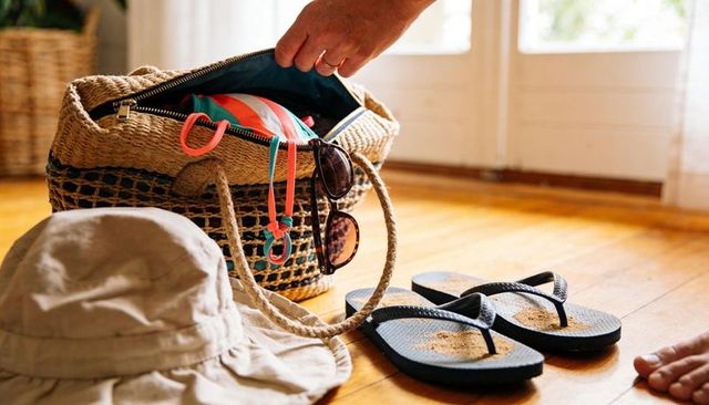 Unpacking summer: straw beach tote revealing swimsuit, sunglasses and sandy flip flops