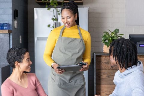 Smiling African American Barista Serving Couple with Tablet POS Reader in Cozy Cafe