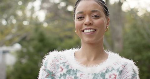 Smiling woman wearing fluffy holiday sweater and gold hoops standing in garden portrait
