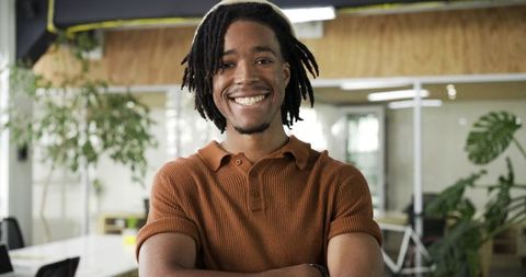 Confident african american man standing arms crossed in modern coworking space with greenery
