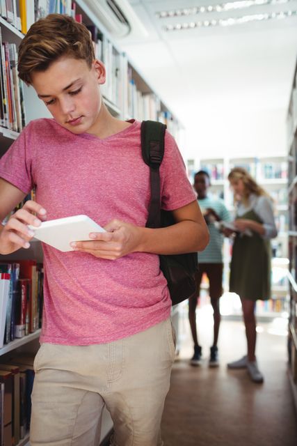 Attentive schoolboy using digital tablet in library at school