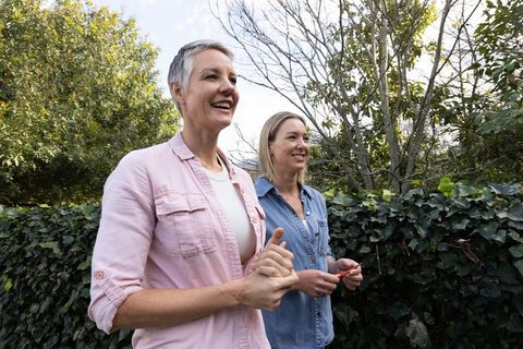 Intergenerational women gardening together pruning ivy hedge in sunlit backyard
