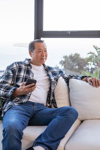 Senior Man Relaxing on Sofa with Smartphone in Modern Living Room
