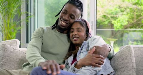 Interracial couple cuddling on sofa at home African American man and Indian woman relaxed