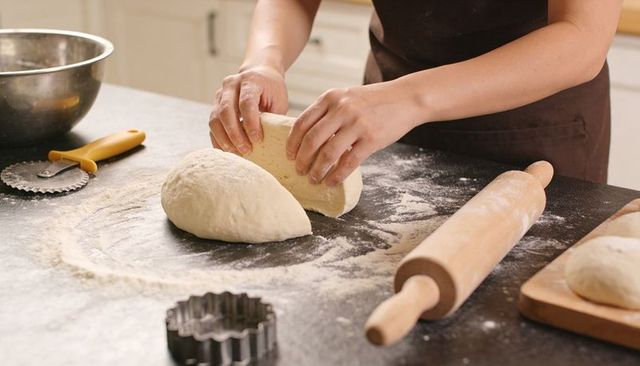 Hands shaping dough on floured counter with rolling pin for artisan bread baking