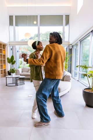 African american couple dancing playfully in bright minimalist glass-walled living room