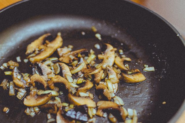 Close-up of mushrooms and onions sautéing in a black pan. Ideal for articles or blogs on cooking techniques, food photography, and recipes.
