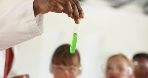 Presenting green test tube to diverse teens wearing goggles in classroom science lesson