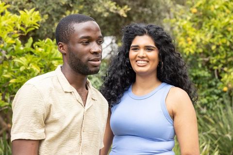 Diverse couple enjoying sunlit backyard among citrus trees, smiling candid lifestyle portrait