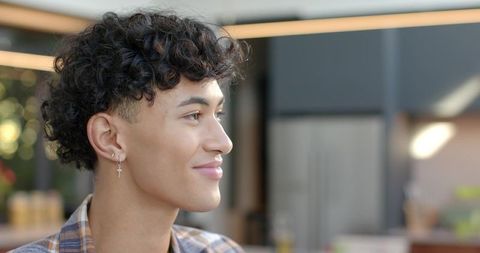 Young man in plaid shirt looking right wearing cross hoop earring in modern kitchen