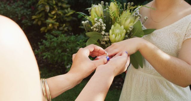 Happy diverse female couple holding bunch of flowers and wearing ring in garden. wedding day and celebration concept.