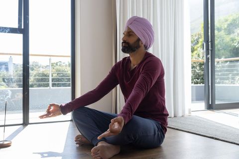 Mid-aged indian man meditating indoors in sunlit room