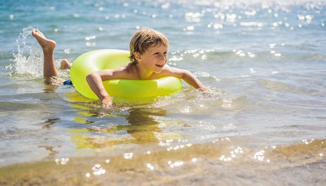 Smiling boy floating on yellow-green inflatable ring in shallow sea with sunlit sparkle