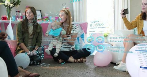 Mother cradling infant at pastel baby shower with friends, balloons, gifts, casual home