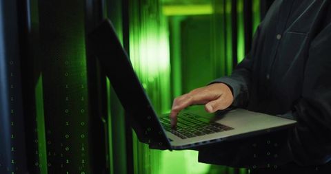 IT Technician Operating Laptop in Data Center with Green LED Lights