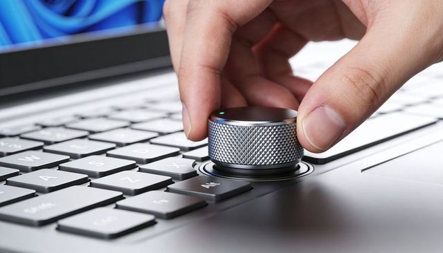 Adjusting knurled metal dial on laptop keyboard for creative workflow and audio control
