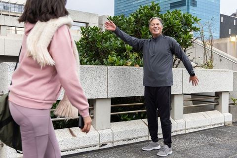 Middle-aged man greeting woman on city terrace during overcast morning walk in activewear