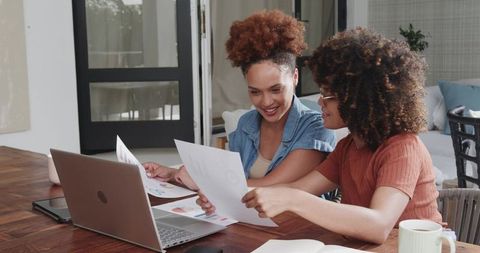 African American women collaborating over charts and laptop in cozy home workspace for learning