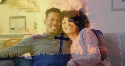 Young couple cuddling on sofa with cross double exposure conveying faith and home warmth