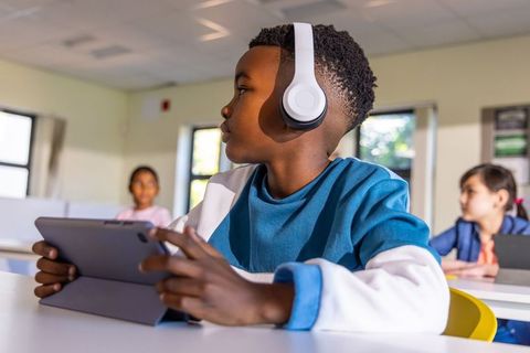 Student wearing headphones using tablet in classroom concentrating on digital lesson