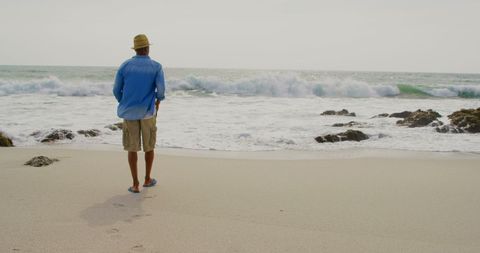 Man in Casual Attire Strolls on Serene Beachfront with Waves - Download Free Stock Images Pikwizard.com