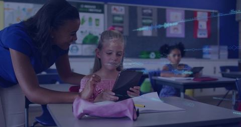 Teacher leaning over guiding student using tablet for interactive learning in classroom