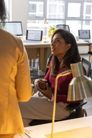 Seated woman tapping smartphone with animated sales charts displaying on monitors in modern office