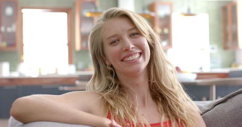 The relaxed and cheerful expression of the young woman captures a welcoming and positive vibe. Perfect for lifestyle blogs, advertisements focused on home décor or cozy ambiances, and promotional materials aimed at youthful energy in domestic settings.