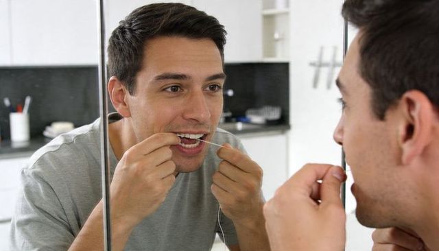 Young man flossing teeth at bathroom mirror during morning personal care routine at home