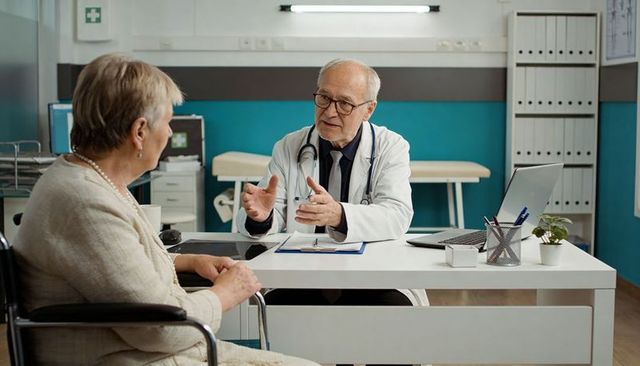 Senior doctor consulting with elderly patient in wheelchair during medical consultation