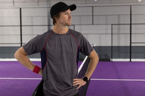 Tennis player standing confidently on purple indoor court wearing cap and wristband