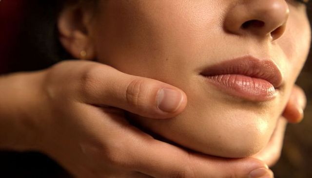Intimate close-up of woman lower face cupping chin and jawline with warm glow