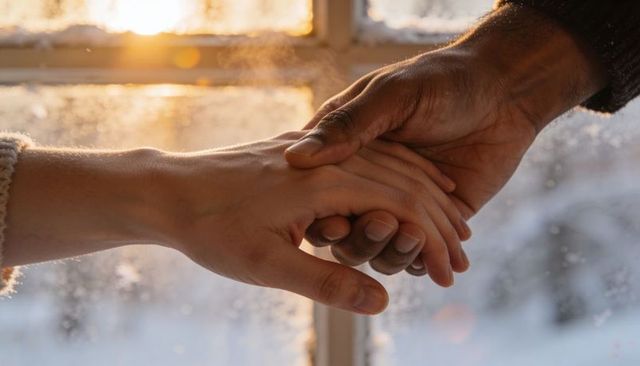 Warmly clasping hands in winter light by frosted window conveying gentle intimacy and comfort