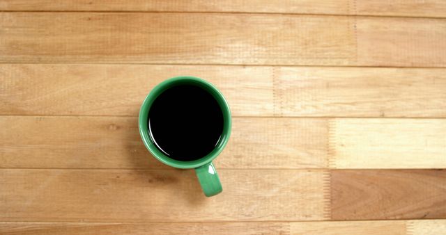 A green mug filled with coffee sits on a wooden surface, with copy space. Its placement offers a simple yet inviting scene for a morning routine or coffee break theme.