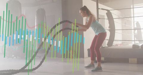 Woman swinging battle ropes in backlit gym with graph overlays for fitness tracking