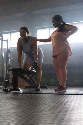 African american women strength training one-arm dumbbell row coaching support