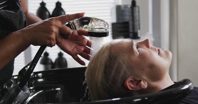 Highlighting personal grooming, beauty treatments, and hair care services, this image captures a detailed moment of a hairstylist rinsing a blonde woman's hair in a salon setting. Useful for marketing beauty services, blogging about hair care tips, or illustrating topics related to personal care and grooming.
