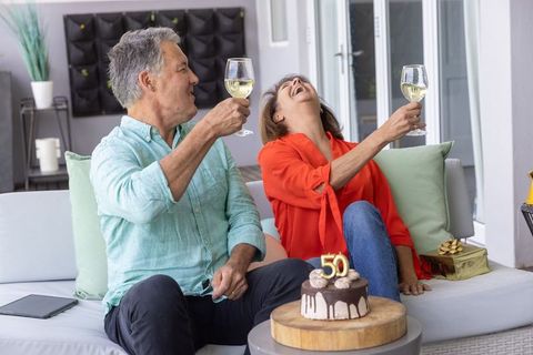 Mature couple celebrating 50th birthday on patio raising wine glasses and laughing together