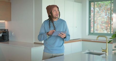 Mid adult man with dreadlocks using tablet in minimalist modern white kitchen interior
