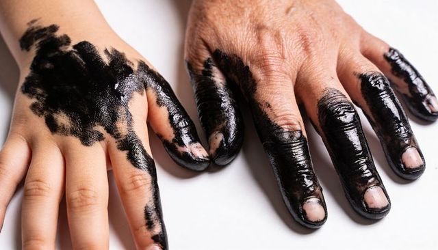 Child and senior hands showing glossy black paint and textured skin close-up