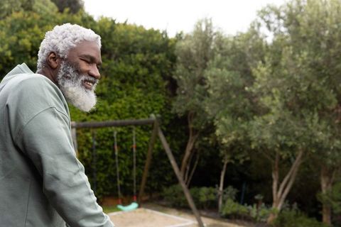 Senior african american man leaning on railing smiling in backyard near swing set