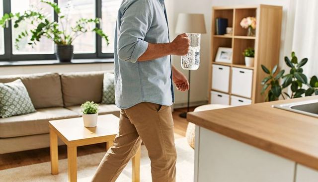 Man walking through cozy minimalist living room carrying glass pitcher of water