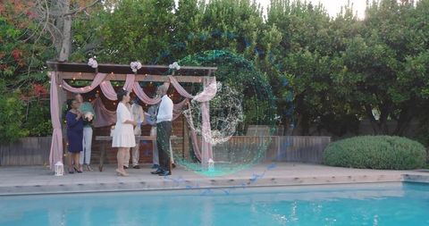 Romantic poolside backyard wedding bride and groom exchanging vows under pink pergola