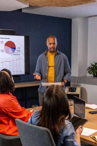 African american presenter sharing revenue charts with diverse team in modern boardroom