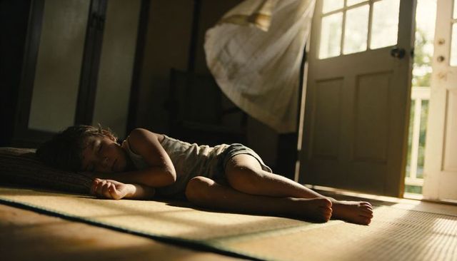 Sunlit boy sleeping on tatami mat near open door with flowing curtain
